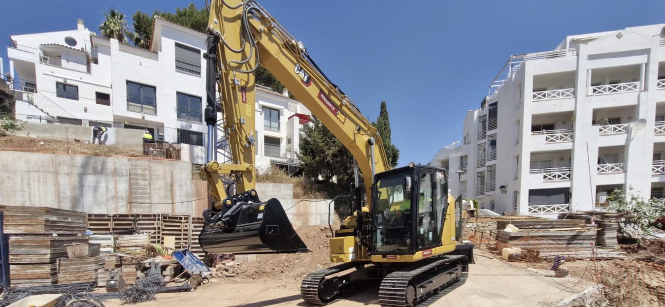Caterpillar CAT crawler excavator rented from Alayan Rentals with raised bucket on a residential construction site near buildings Alayan Alquileres