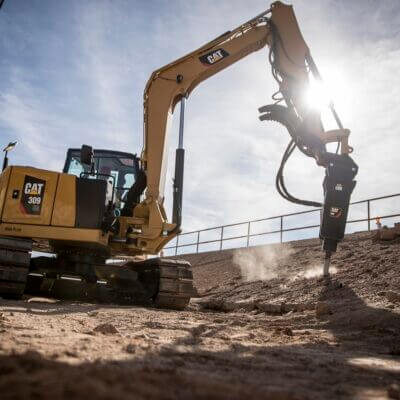 Escavatore Caterpillar a noleggio al lavoro con martello durante un lavoro di manutenzione del verde Alayan (CGTE) Noleggio