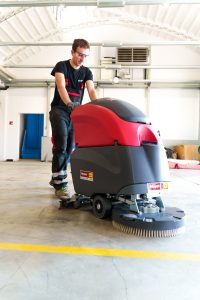 Bediener bei der Arbeit mit einer professionellen Nachläufer-Scheuersaugmaschine zur Miete von Alayan Rentals in einer Industriehalle