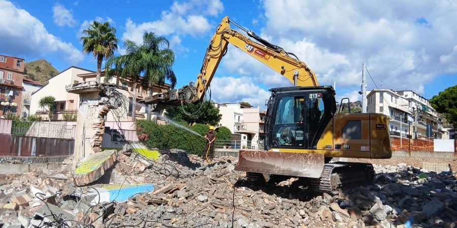 Rental Caterpillar CAT 313 GC crawler excavator by Alayan Rentals with hydraulic crusher engaged in a demolition site with dust suppression.