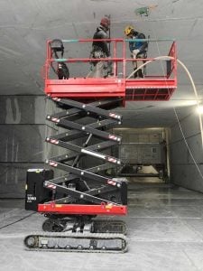 Piattaforma aerea a forbice cingolata Almac Bibi 1090 EVO a noleggio Alayan Rentals con operatori al lavoro a soffitto in ambiente industriale