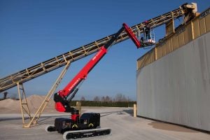 Piattaforma aerea telescopica cingolata AlmaCrawler Jibbi 1670 EVO a noleggio Alayan Rentals con operatore al lavoro su un nastro trasportatore industriale