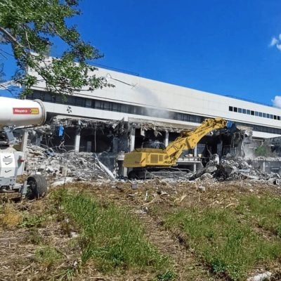 Rental crawler excavator by Alayan Rentals engaged in the demolition of an industrial building using a water dust suppression system.
