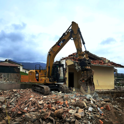 Rental Caterpillar CAT 316F crawler excavator by Alayan Rentals equipped with a hydraulic crushing shear during building demolition.