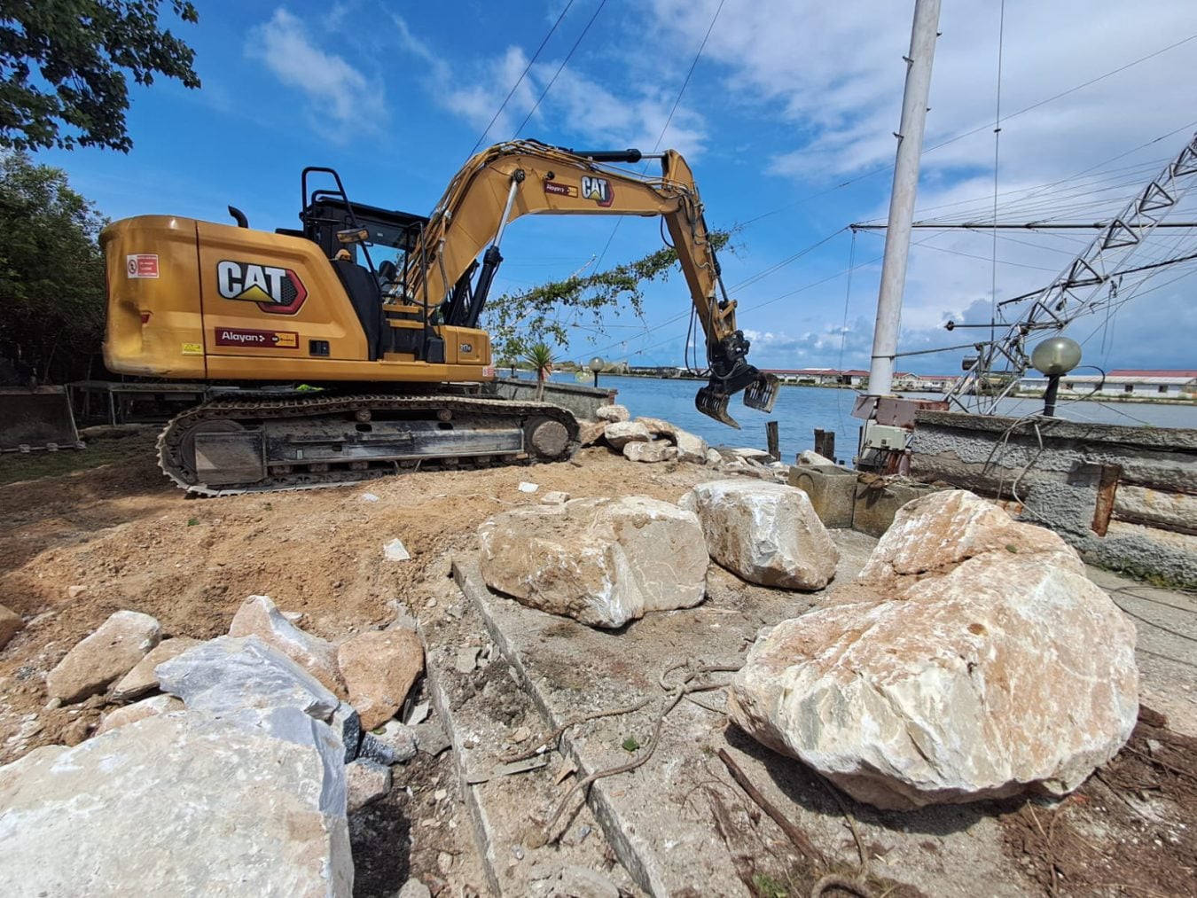 Escavatore cingolato Caterpillar CAT 317 a noleggio Alayan Rentals con pinza selezionatrice di massi al lavoro per la messa in sicurezza della scogliera lungo la costa Alayan Rental