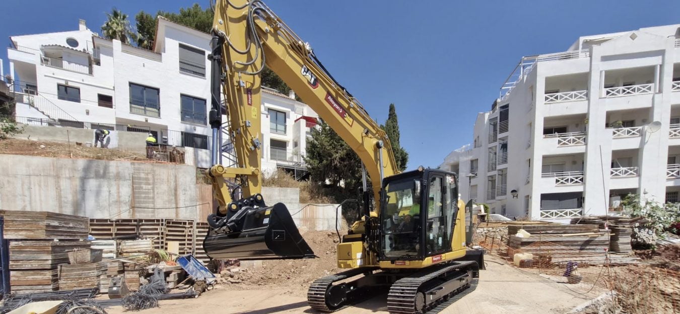 Escavatore cingolato Caterpillar CAT a noleggio Alayan Rentals con benna alzata in un cantiere edile residenziale vicino a degli edifici Alayan Rental