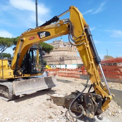 Rental Caterpillar crawler excavator by Alayan Rentals operating on a construction site in the historic center of Rome with Castel Sant'Angelo in the background.