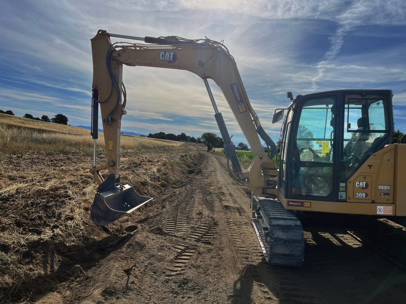 Miniescavatore cingolato Caterpillar CAT 309 a noleggio Alayan Rentals posizionato lungo un tracciato di campagna per scavi e movimento terra Alayan Rental