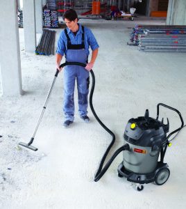 Operator in work overalls using a 65L wheeled industrial vacuum cleaner for rent by Alayan Rentals to clean a job site floor