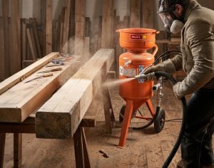 Bediener mit Schutzmaske bei der Arbeit mit einem Profi-Sandstrahlgerät zur Miete von Alayan Rentals zur Reinigung eines Holzbalkens