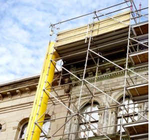 Yellow rubble discharge chute tube installed on building renovation scaffolding by Alayan Rentals