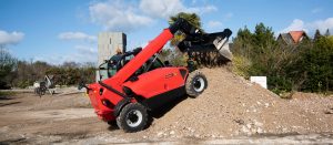 Sollevatore telescopico fisso Manitou rosso con benna scarica terra e inerti su un cumulo in cantiere a noleggio Alayan Rentals