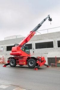 Roter drehbarer Manitou Teleskopstapler stabilisiert vor einem im Bau befindlichen Gebäude mit ausgefahrenem Ausleger und Hakenwinde zur Miete - Alayan Rentals