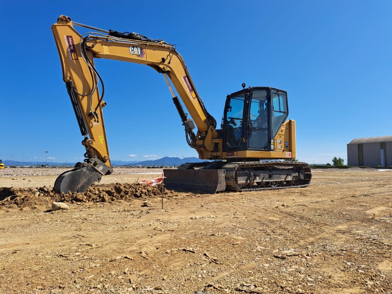 Escavatore cingolato giallo Caterpillar CAT 309 CR a noleggio Alayan Rentals con la benna nel terreno durante uno scavo in cantiere Alayan Noleggio