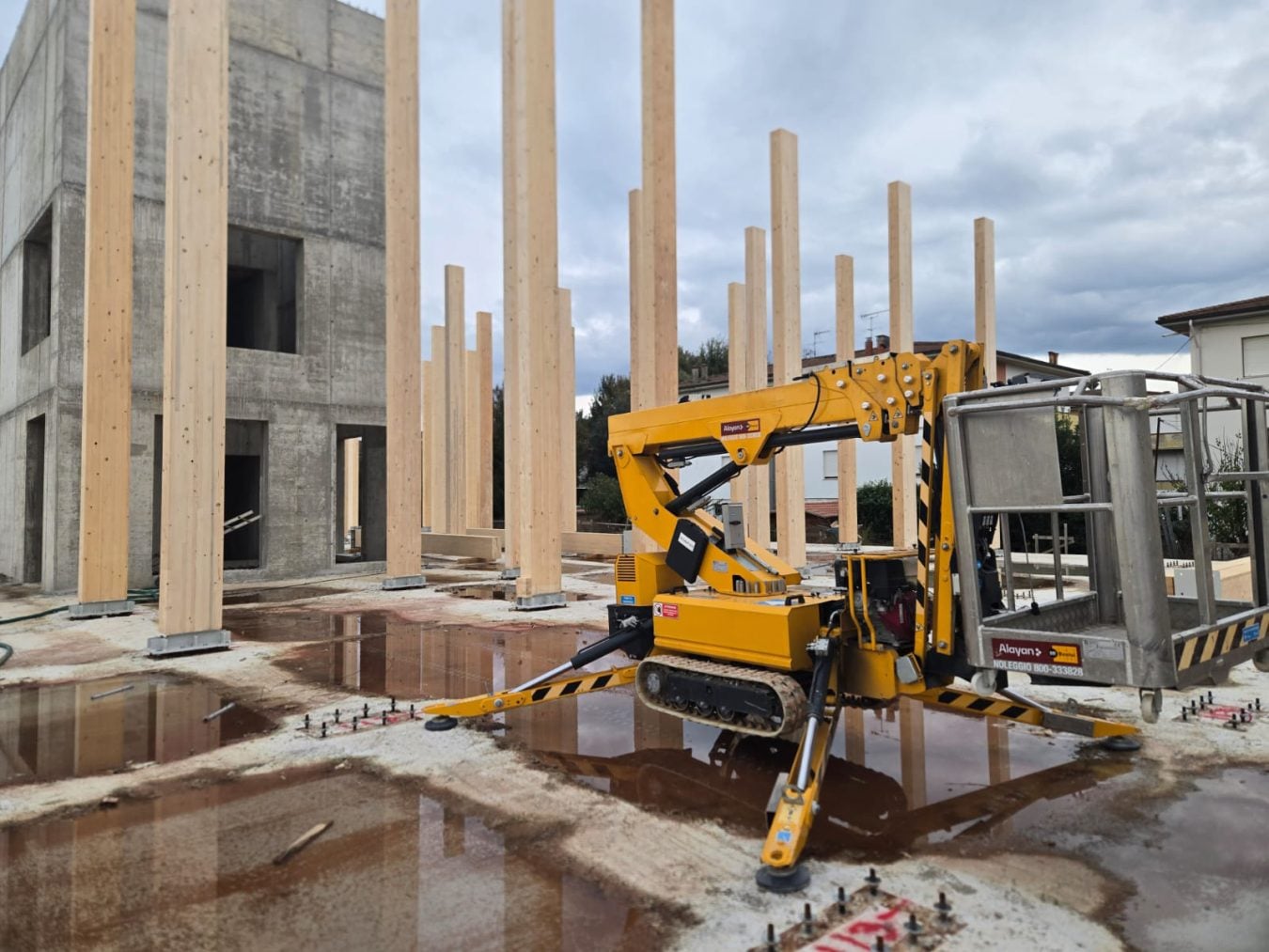 Piattaforma aerea ragno cingolata gialla a noleggio Alayan Rentals, stabilizzata in un cantiere di costruzioni in legno Alayan Noleggio