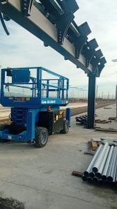 Piattaforma aerea verticale a pantografo Genie GS-3246 elettrica blu posizionata all'interno di un cantiere indoor per montaggio cartongesso a noleggio Alayan Rentals