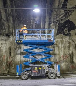 Piattaforma aerea verticale a pantografo Genie GS-3369 RT fuoristrada 4x4 blu posizionata presso un cantiere di infrastrutture ferroviarie a noleggio Alayan Rentals
