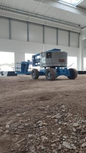 Blue 4x4 Genie Z-45 rough-terrain articulated boom lift operating inside a warehouse under construction for rent – Alayan Rentals