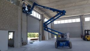 Piattaforma aerea articolata elettrica Genie Z-45 blu in opera all'interno di un capannone industriale a noleggio Alayan Rentals