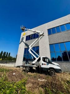 Piattaforma aerea autocarrata articolata su Iveco Daily con braccio esteso in opera per manutenzione facciata edificio commerciale a noleggio Alayan Rentals
