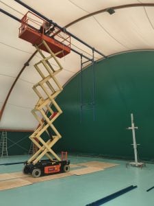 Ausgefahrene orange Elektro-Scherenarbeitsbühne JLG 4069LE mit Bediener beim Einsatz in einer Traglufthalle zur Miete – Alayan Rentals